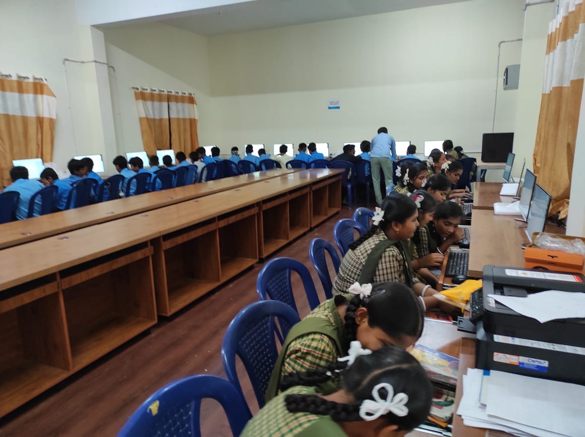 Students in blue chairs working at rows of desktop computers in a large lab