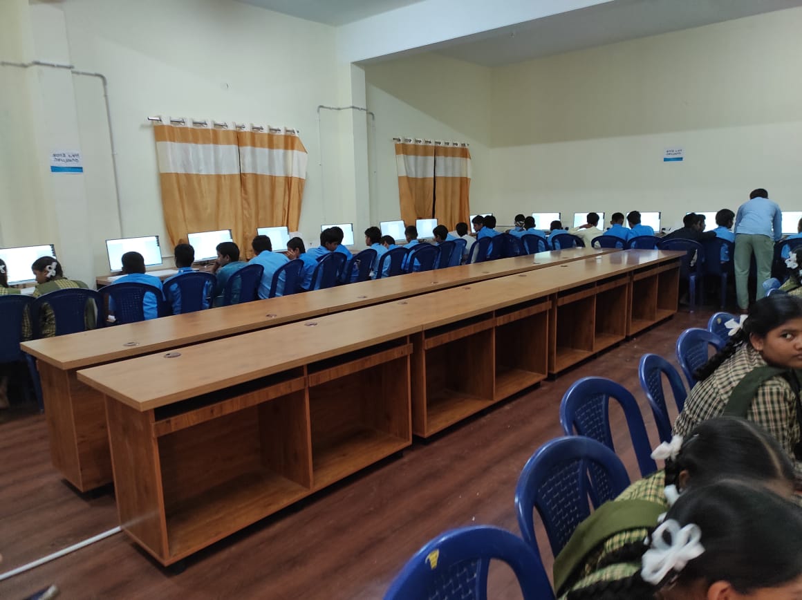 Rows of students at computers along the walls of the lab, with an instructor standing