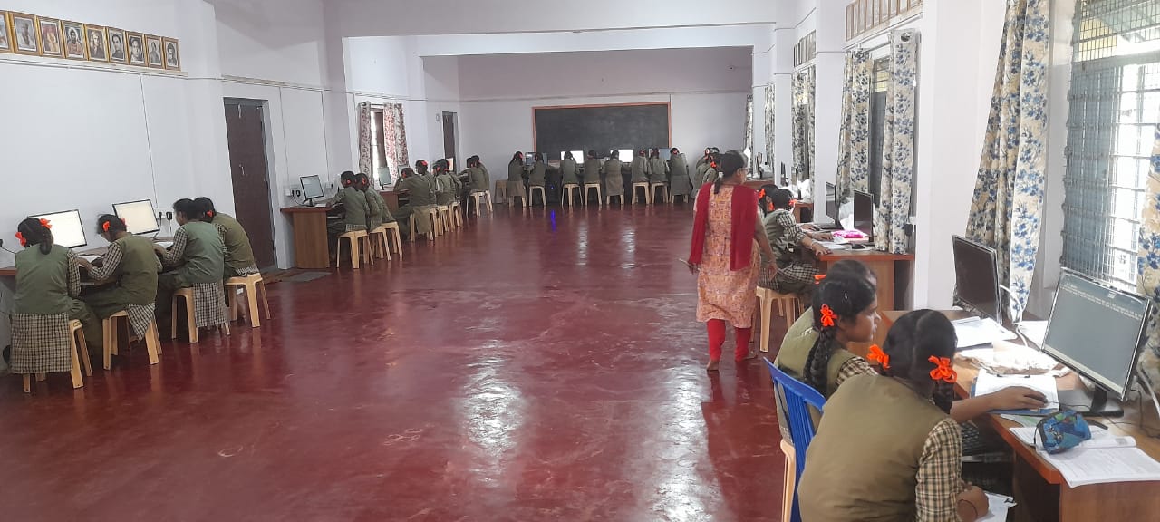 Girls in green uniforms at computers in a long hall