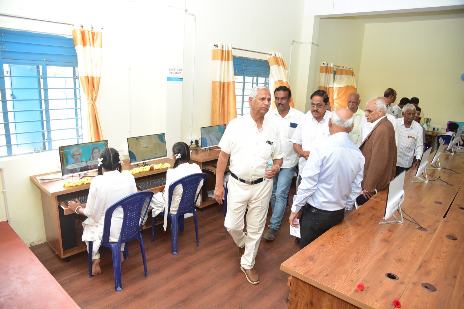 A row of students at computers along the lab wall, with visitors walking through