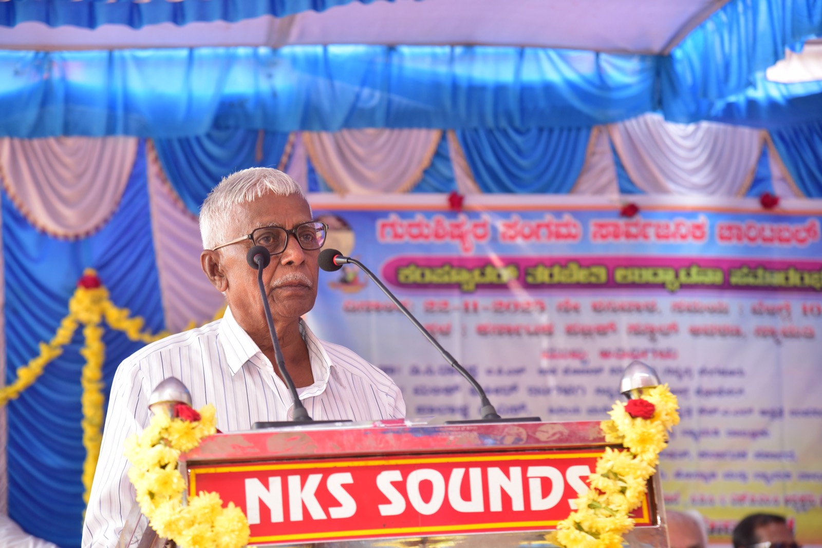 A guest addressing the gathering from a flower-decked podium beneath the Trust's banner