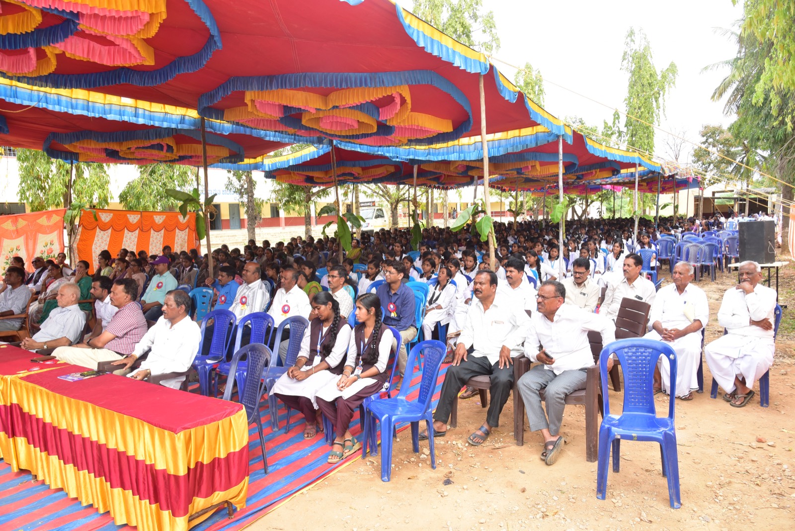 Students and villagers seated beneath a large decorated canopy