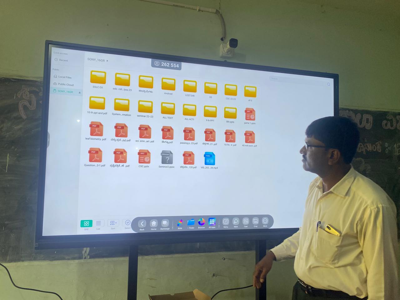 A teacher looking at folders and documents on a large wall-mounted smart board